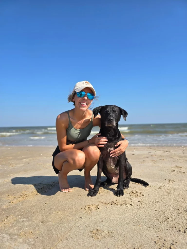 DFW dog trainer with military background next to black dog on beach.