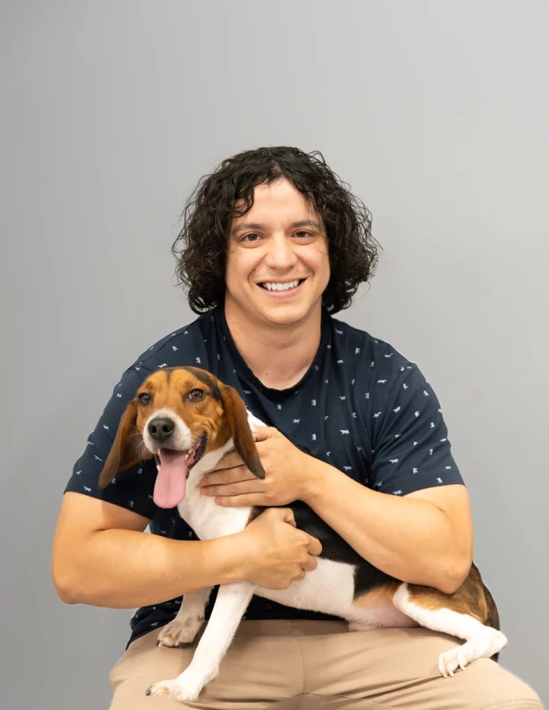 Sam, military veteran and expert dog trainer at OLK9 DFW, smiling while holding a happy Beagle in Dallas-Fort Worth
